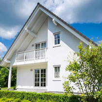 Ein Giebel eines weißen Steildachhauses mit Logia und einer grünen Hecke im Vordergrund