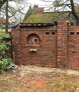 Eine im Bau befindliche Mauer mit Aussparrung für einen zukünftige Brunnen in rotem Klinker